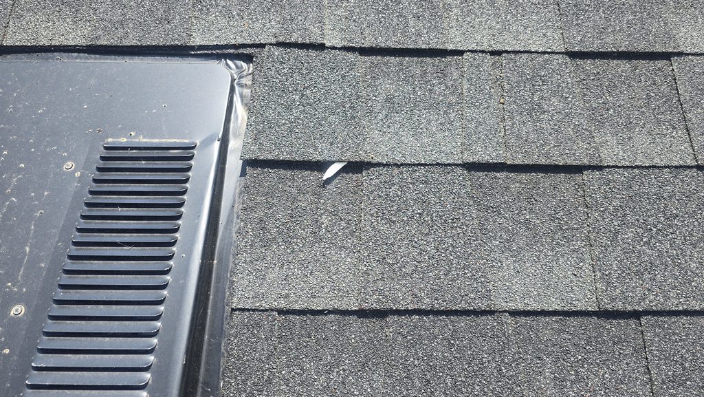 Small piece of shingle packaging caught beneath a GAF Timberline shingle near an O'Hagin roof vent